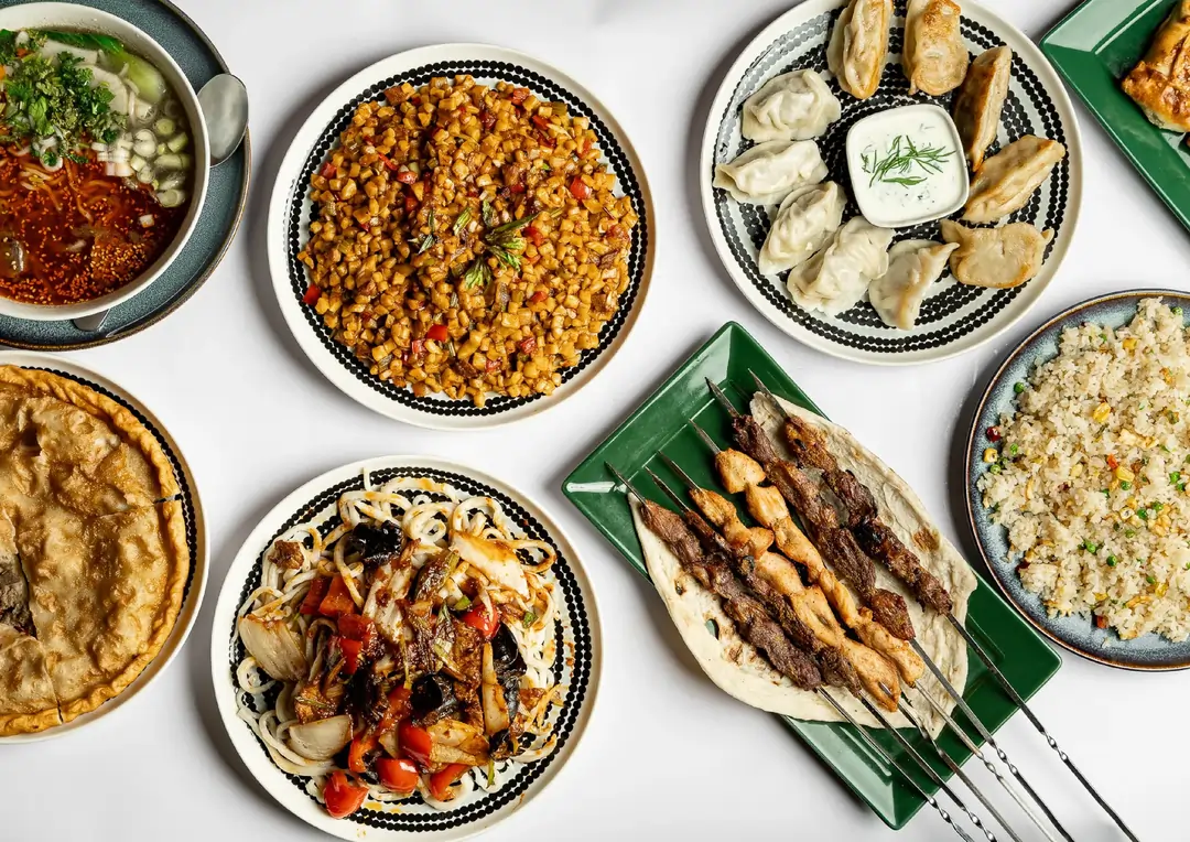 Assorted dishes including dumplings with dipping sauce, grilled meat skewers on flatbread, noodles with vegetables, fried rice, pot pie, diced vegetable stir-fry, and soup with greens and broth on a white background.